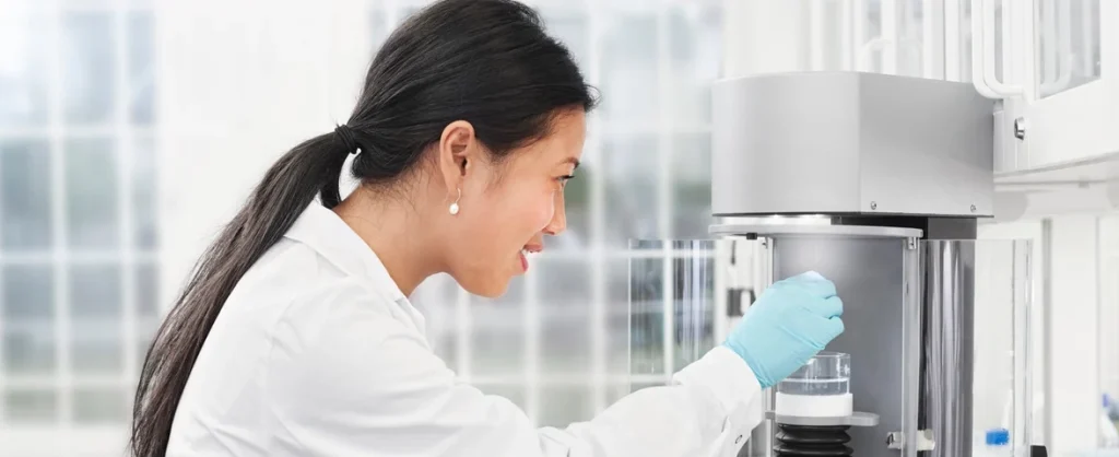 A woman in lab coat and latex gloves placing a sample into a measurement device.