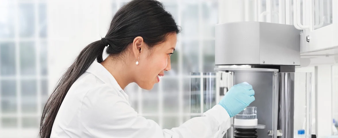 A woman in lab coat and latex gloves placing a sample into a measurement device.