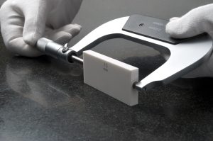White-gloved hands calibrating a micrometer using a ceramic gauge block.