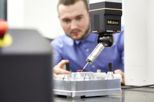 A person uses a ruby probe CMM to measure a metal part.