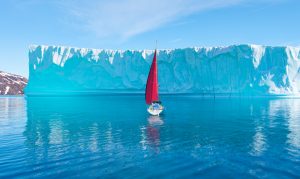 A sailboat on calm water next to a glacier.