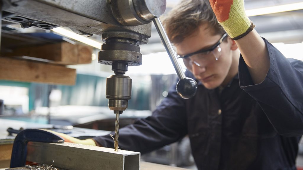 A person using an industrial machine to create a hole in a metal part.