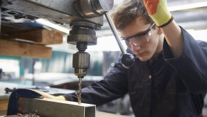 A person using an industrial machine to create a hole in a metal part.